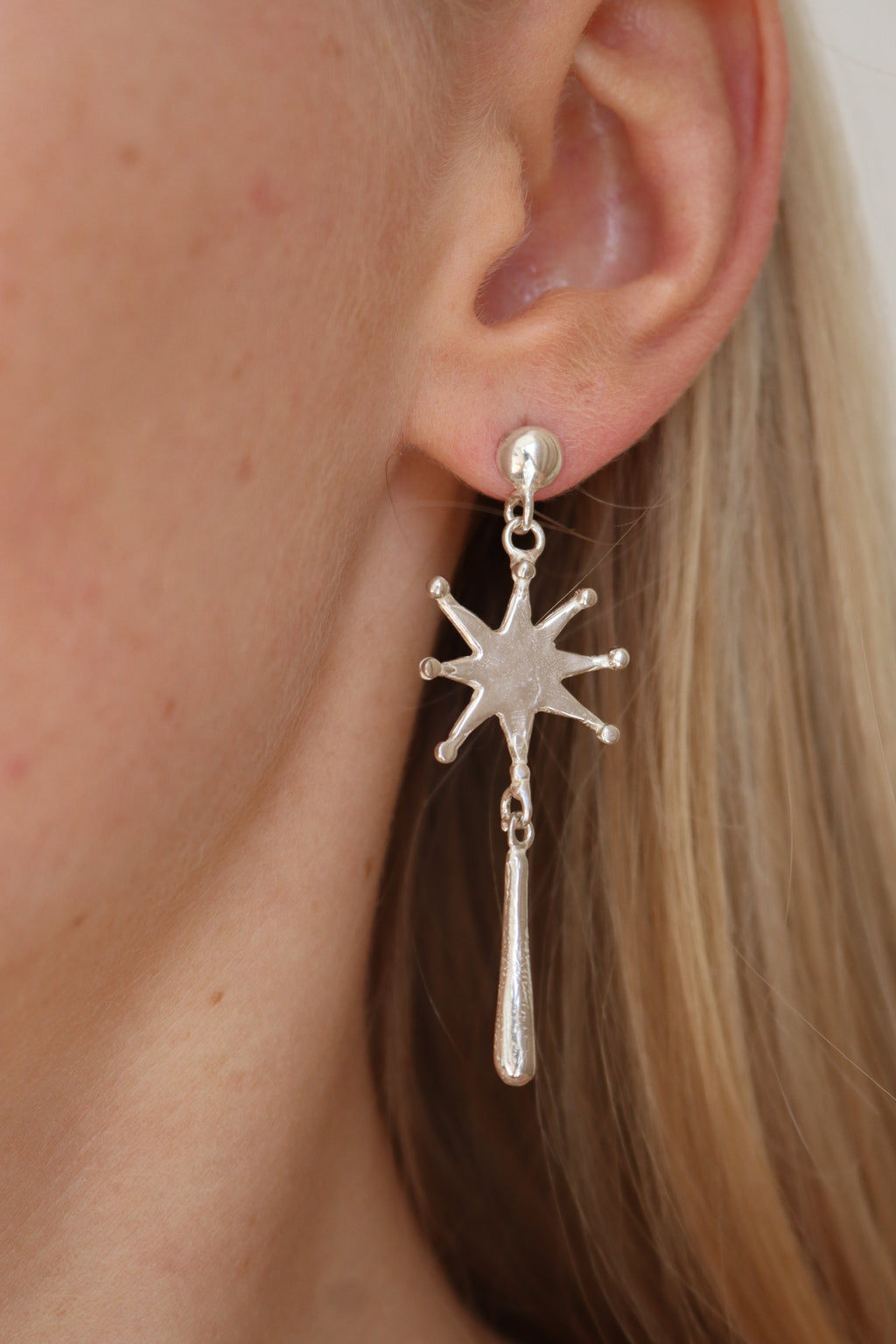 Silver star-shaped earring worn by a person with blonde hair.